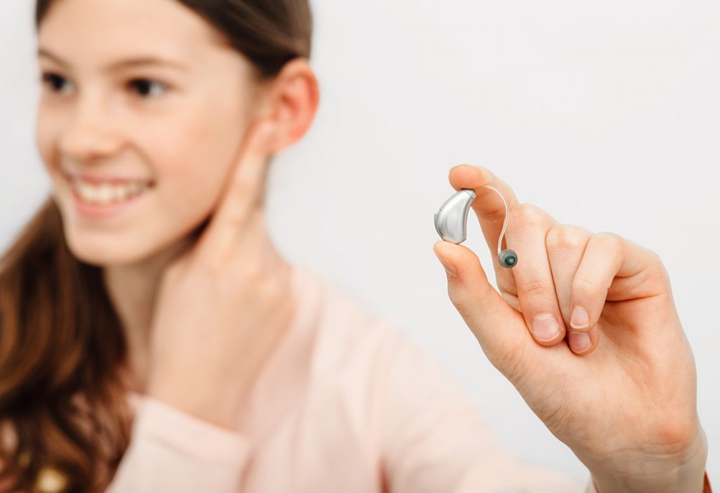 Hearing solution for children. Girl holding a hearing aid, treatment of deafness in children.